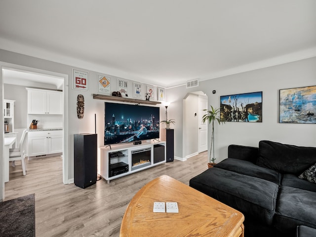 living area featuring visible vents, arched walkways, light wood finished floors, and baseboards