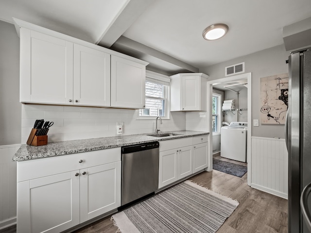kitchen with appliances with stainless steel finishes, a sink, a wainscoted wall, washer / dryer, and visible vents