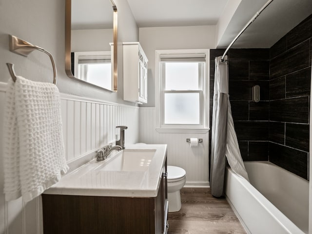 full bathroom featuring shower / bath combination with curtain, wood finished floors, a wainscoted wall, vanity, and toilet