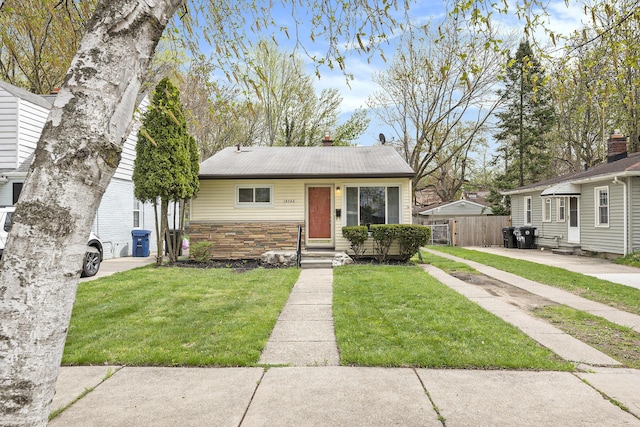 bungalow-style home with entry steps, a front yard, fence, and stone siding