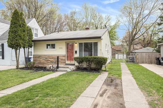 view of front of home with stone siding, fence, a gate, and a front yard