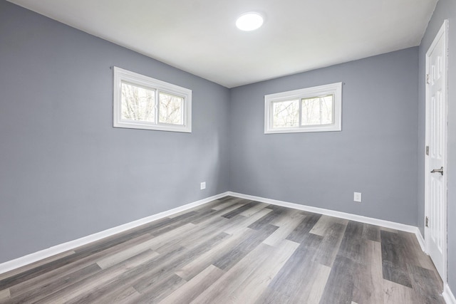 spare room featuring baseboards, wood finished floors, and a wealth of natural light