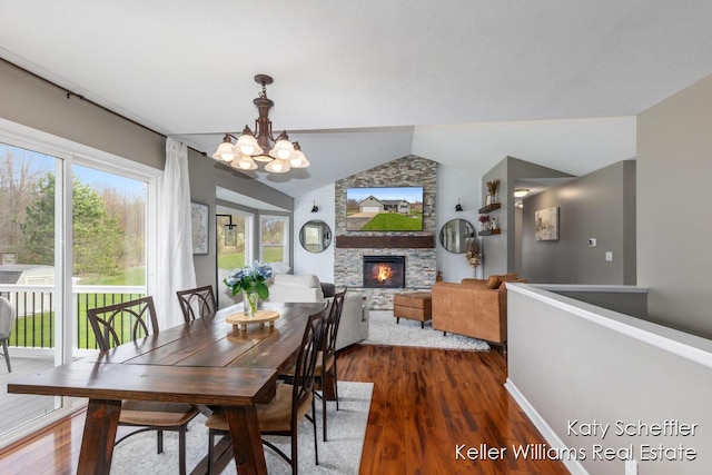 dining area featuring a chandelier, a stone fireplace, dark wood finished floors, baseboards, and vaulted ceiling