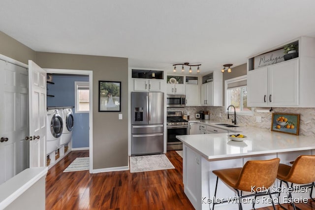 kitchen featuring appliances with stainless steel finishes, a sink, separate washer and dryer, a peninsula, and dark wood-type flooring