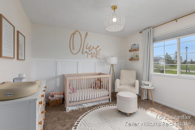 carpeted bedroom with a sink, a crib, a decorative wall, and wainscoting