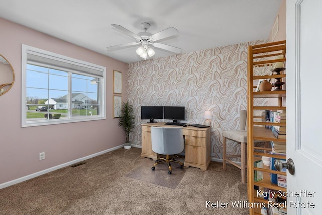 carpeted home office with a ceiling fan, visible vents, baseboards, an accent wall, and wallpapered walls