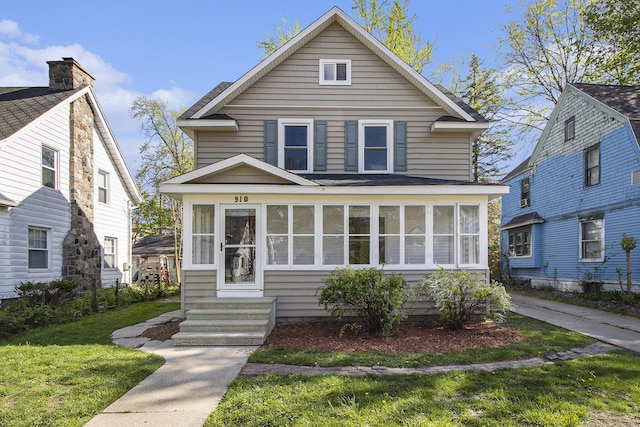 american foursquare style home featuring entry steps, a sunroom, and a front yard