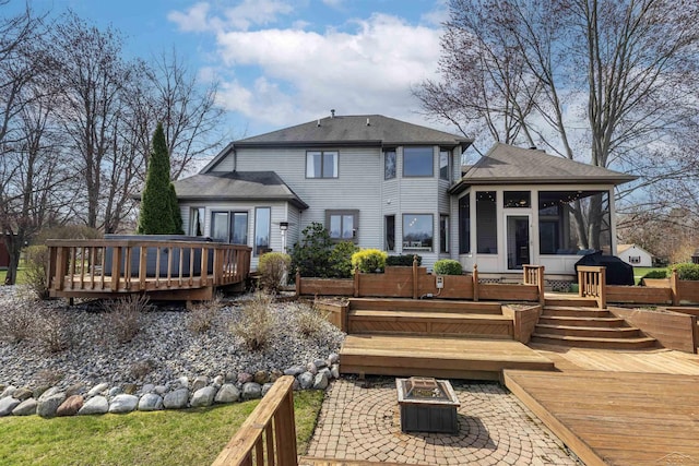 rear view of house with a fire pit, a deck, a patio, a sunroom, and a shingled roof