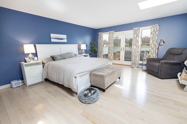 bedroom with a skylight, access to exterior, baseboards, and light wood-type flooring