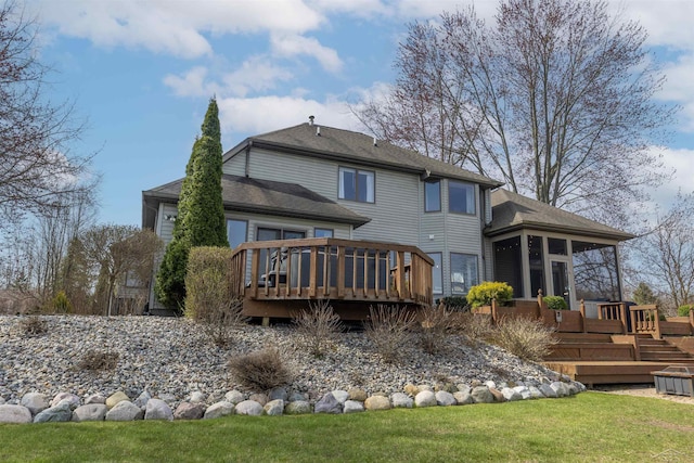 back of property with a lawn, a deck, a sunroom, and roof with shingles
