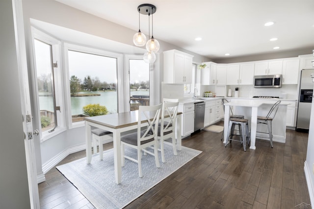 dining room with recessed lighting, a water view, baseboards, and dark wood-style floors