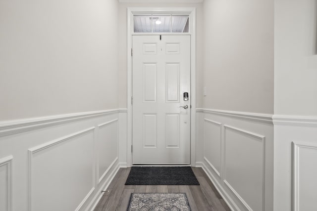 doorway with wainscoting, a decorative wall, and dark wood-type flooring