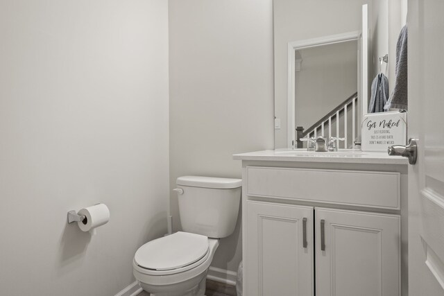 half bathroom with toilet, baseboards, and vanity