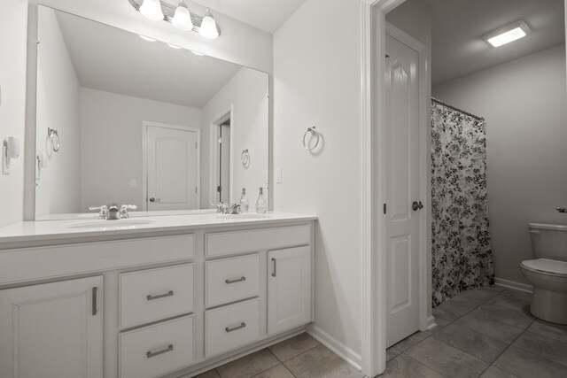 full bath featuring double vanity, a sink, tile patterned flooring, and toilet