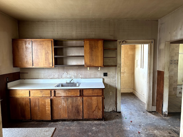 kitchen with open shelves, a sink, brown cabinets, and unfinished concrete floors