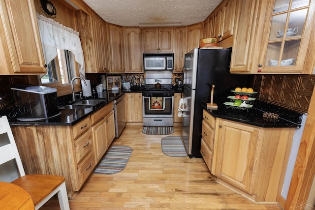 kitchen featuring decorative backsplash, a textured ceiling, a sink, stainless steel appliances, and light wood-style flooring