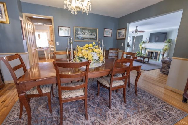 dining room featuring baseboards, ceiling fan with notable chandelier, a glass covered fireplace, and wood finished floors