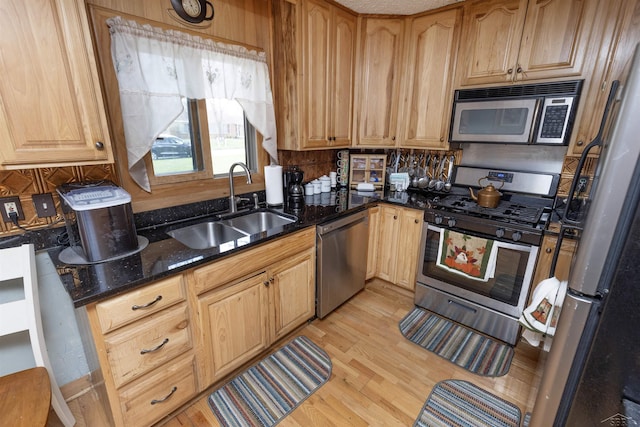 kitchen with a sink, light wood-style floors, dark stone counters, stainless steel appliances, and decorative backsplash