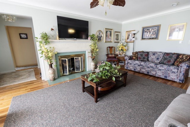 living room with a glass covered fireplace, ceiling fan, wood finished floors, and crown molding