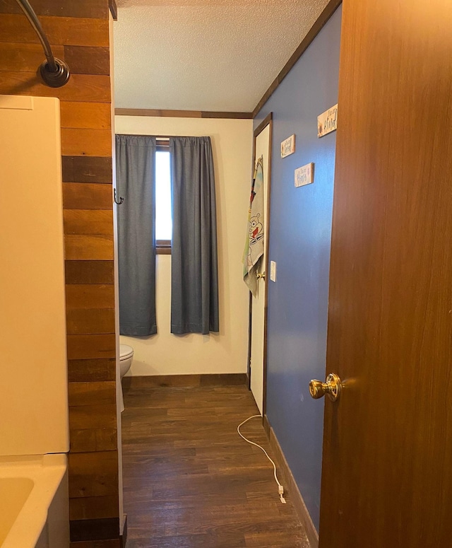 hall featuring baseboards, ornamental molding, a textured ceiling, and dark wood-style floors