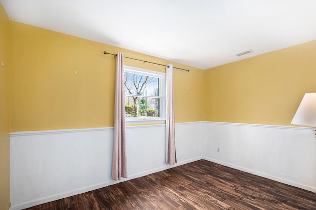 empty room featuring baseboards, wood finished floors, and visible vents
