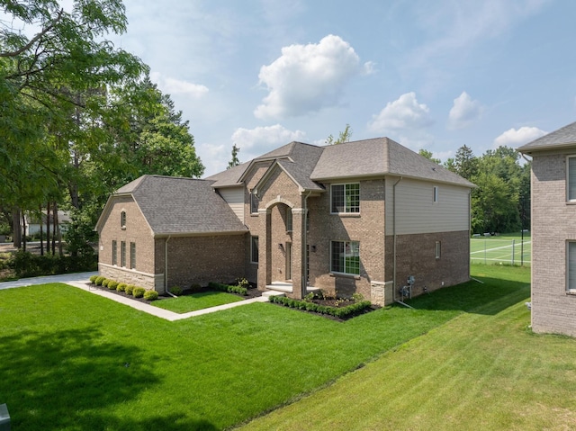 view of front of property with a shingled roof, a front lawn, and brick siding