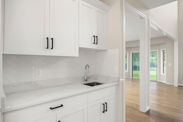 kitchen with white cabinets, light stone counters, a sink, light wood-type flooring, and tasteful backsplash