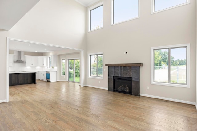 unfurnished living room with visible vents, a towering ceiling, baseboards, light wood-type flooring, and a tile fireplace
