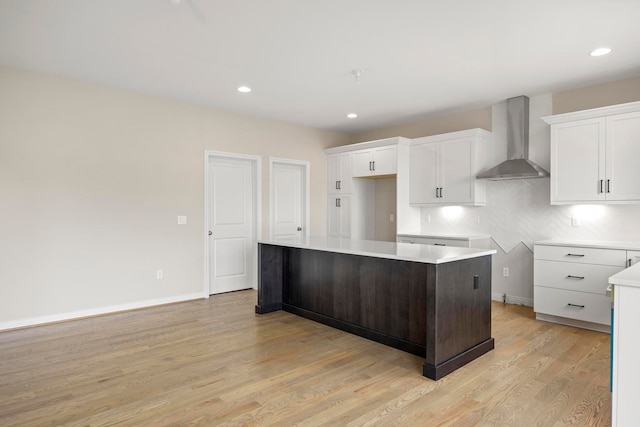 kitchen featuring wall chimney range hood, white cabinets, light wood-style flooring, a center island, and recessed lighting