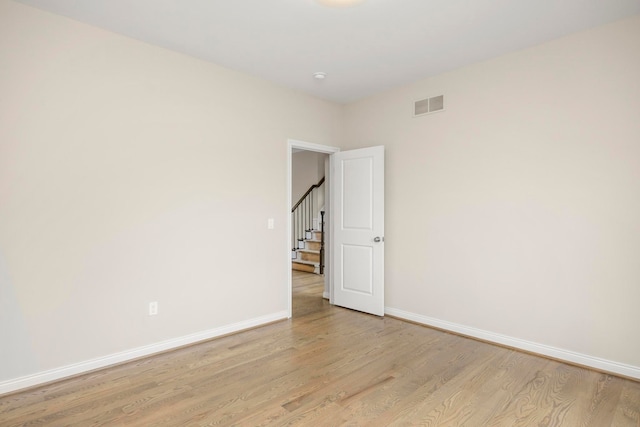 empty room with baseboards, stairs, light wood-style flooring, and visible vents