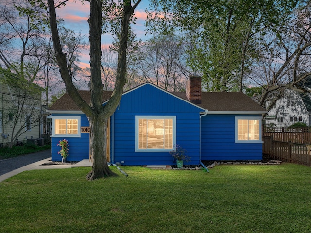 view of front of property with a shingled roof, fence, a yard, and a chimney