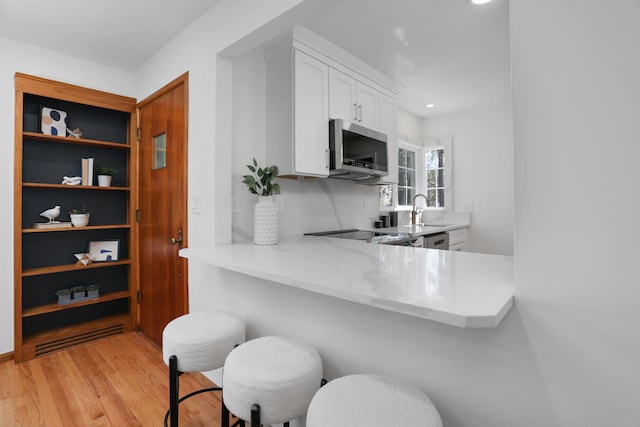 kitchen featuring a breakfast bar, a sink, light wood-style floors, white cabinetry, and stainless steel microwave