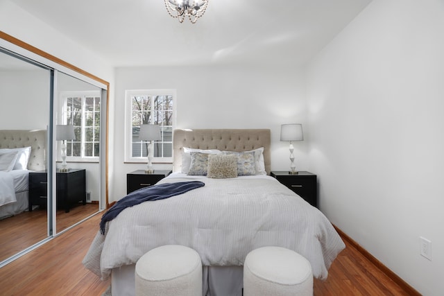 bedroom with a closet, baseboards, wood finished floors, and an inviting chandelier