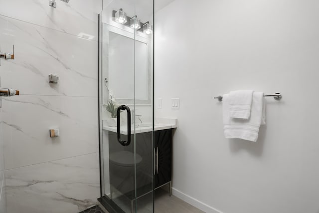 bathroom with baseboards, a marble finish shower, and vanity