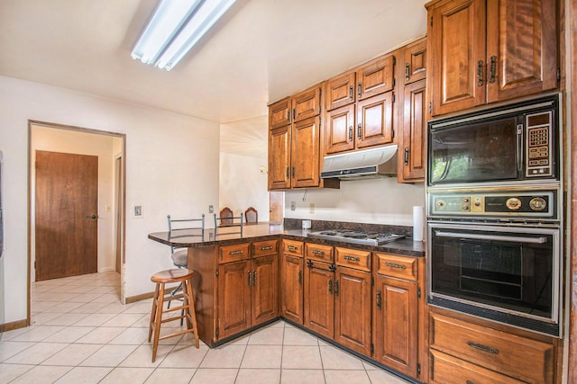 kitchen with brown cabinetry, black microwave, a peninsula, stainless steel stovetop, and oven