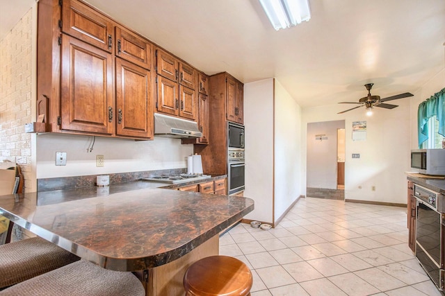 kitchen featuring dark countertops, a breakfast bar, brown cabinetry, stainless steel appliances, and under cabinet range hood