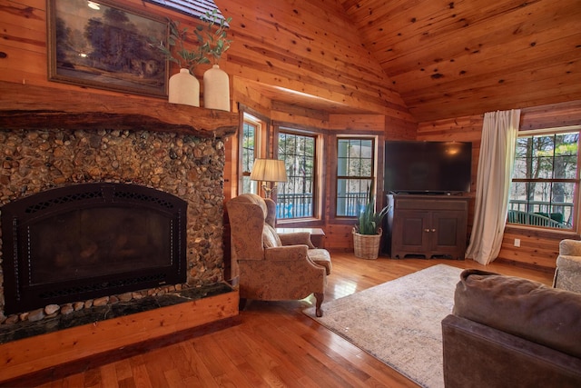 living area featuring wooden walls, high vaulted ceiling, a stone fireplace, and hardwood / wood-style flooring