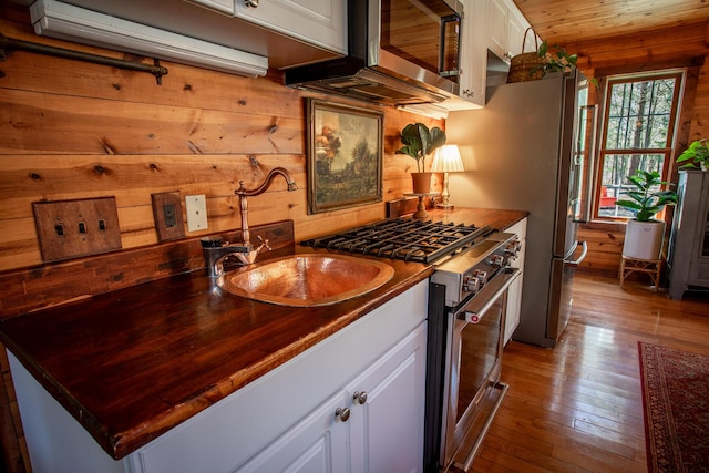 kitchen featuring white cabinets, wooden walls, appliances with stainless steel finishes, a sink, and hardwood / wood-style floors