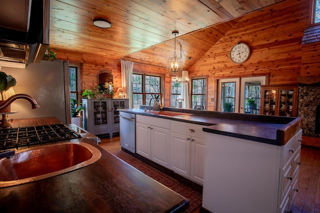 kitchen featuring stainless steel dishwasher, dark countertops, wood walls, and a sink