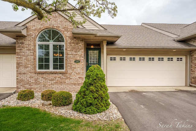 ranch-style house with brick siding, a garage, roof with shingles, and driveway