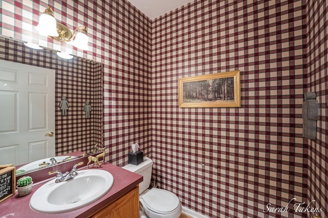 bathroom featuring vanity, toilet, and wallpapered walls