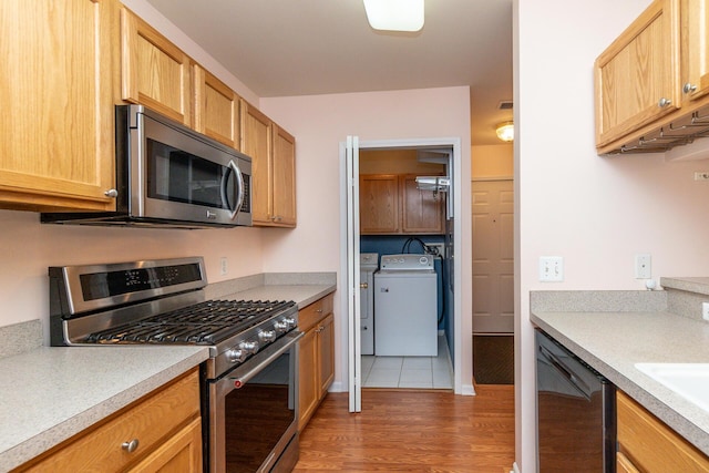 kitchen featuring appliances with stainless steel finishes, light wood-type flooring, light countertops, a sink, and separate washer and dryer