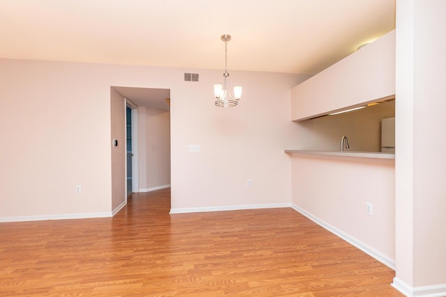unfurnished dining area featuring visible vents, an inviting chandelier, baseboards, a sink, and light wood finished floors