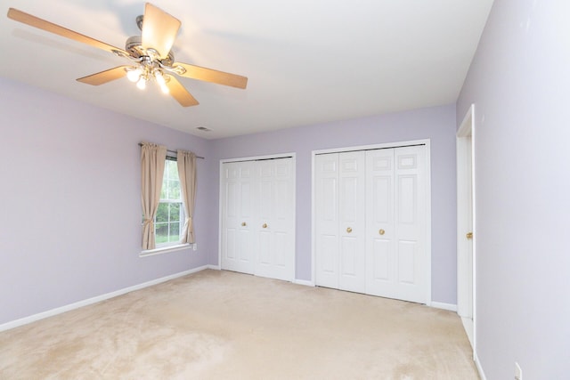 unfurnished bedroom featuring light colored carpet, multiple closets, and baseboards
