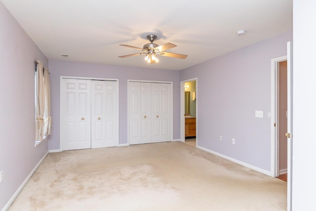 unfurnished bedroom with two closets, baseboards, light carpet, and ensuite bath
