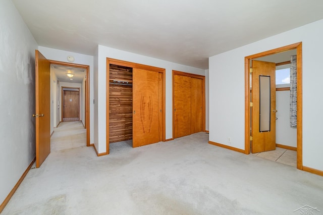 unfurnished bedroom featuring baseboards, multiple closets, and light carpet