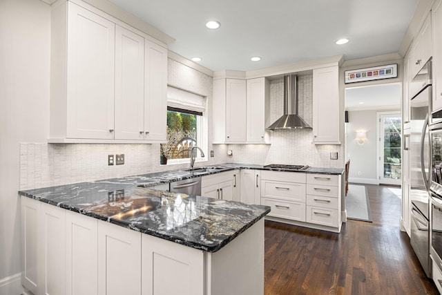 kitchen with a peninsula, wall chimney range hood, a sink, appliances with stainless steel finishes, and a wealth of natural light