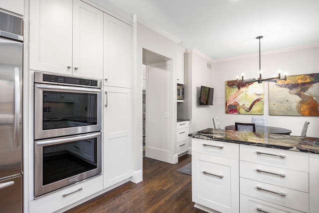 kitchen with ornamental molding, dark wood-style floors, dark stone counters, white cabinets, and appliances with stainless steel finishes