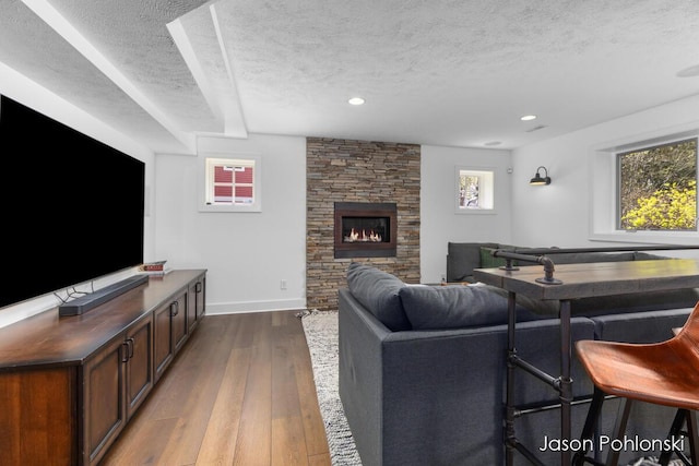 living room with a stone fireplace, recessed lighting, a textured ceiling, and dark wood-style floors