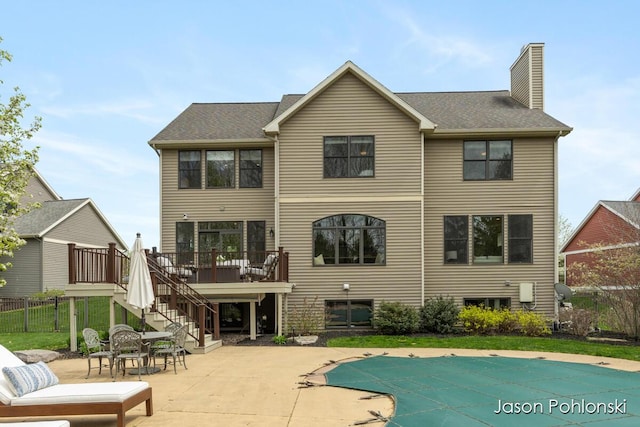 rear view of house with a chimney, a wooden deck, a patio area, a fenced in pool, and stairs